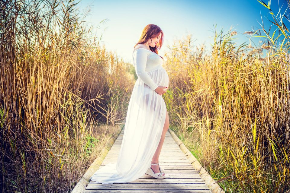 Retrato de una mujer embarazada con vestido blanco largo.