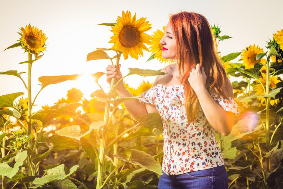 Retrato de una mujer entre girasoles al atardecer.