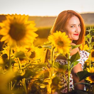 A red-haired woman is pictured among sunflowers in a field bathed in warm evening light.