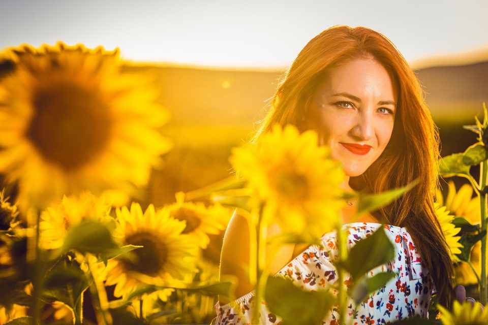 A smiling woman is pictured among sunflowers, illuminated by a warm golden light.