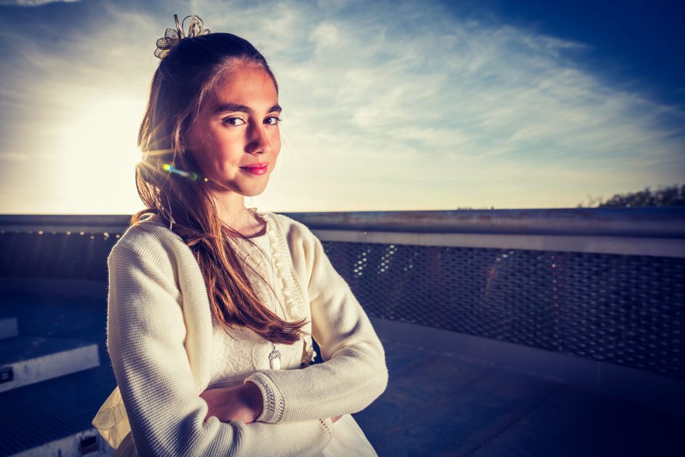 Retrato de una niña con vestido blanco, chaqueta de punto y adorno en el cabello.