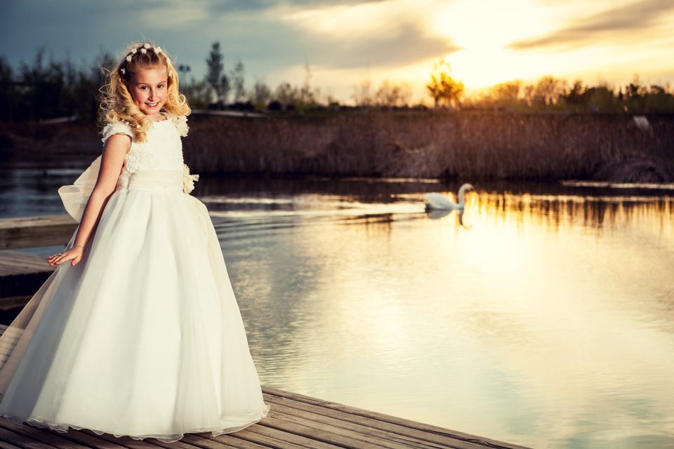 Retrato de una niña con vestido blanco de comunión y una corona floral.