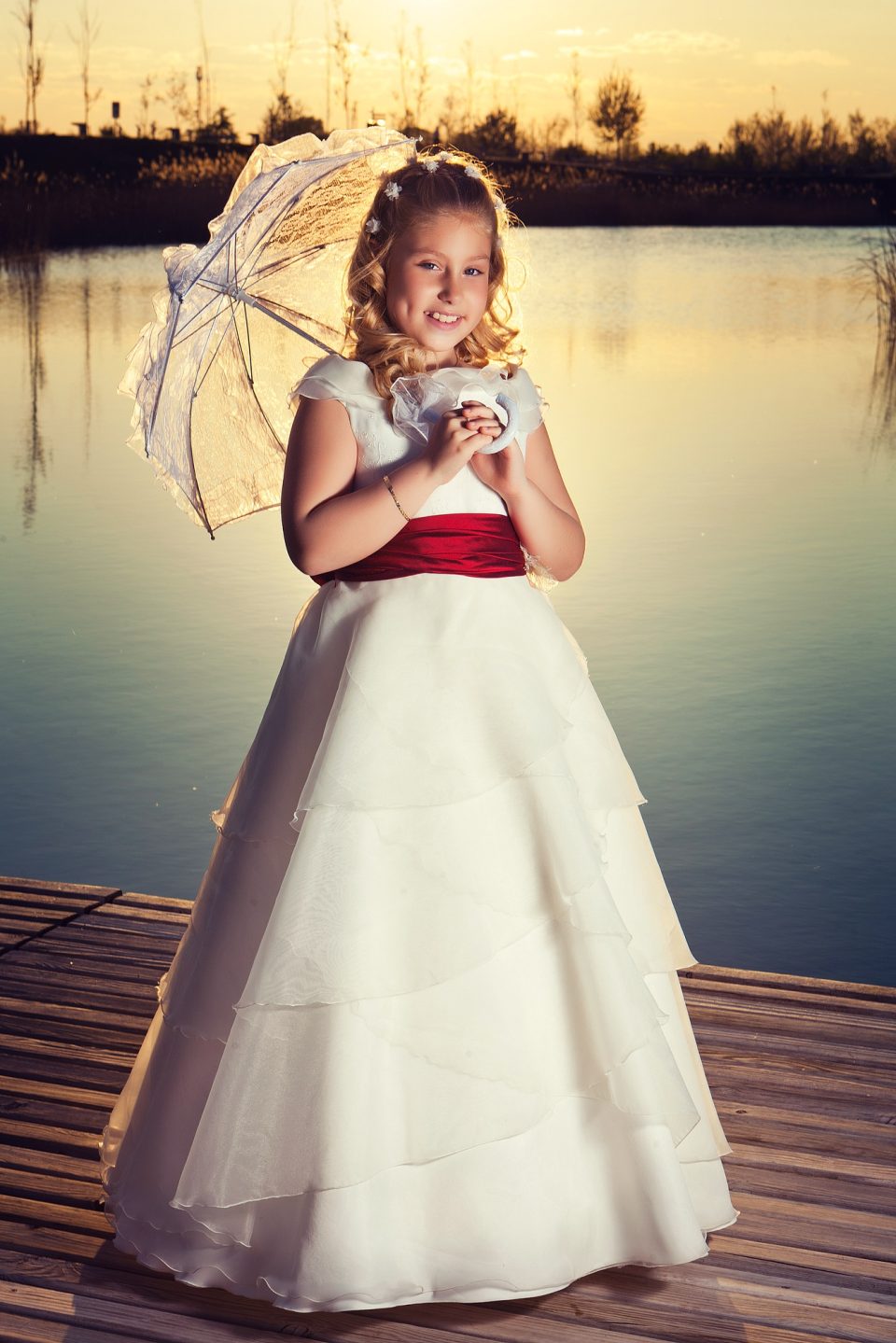 Retrato de una niña con vestido blanco y fajín rojo.
