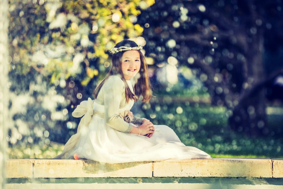 Retrato de una niña sentada en el borde de una fuente o estructura de piedra en un parque.
