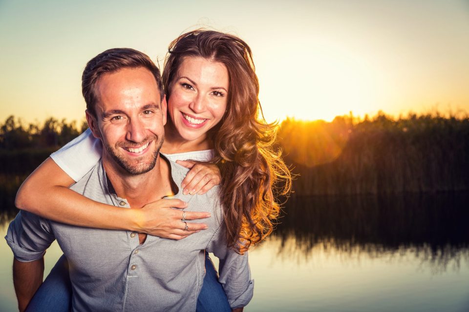 Retrato de una pareja sonriente junto a un estanque en un parque, durante un atardecer.