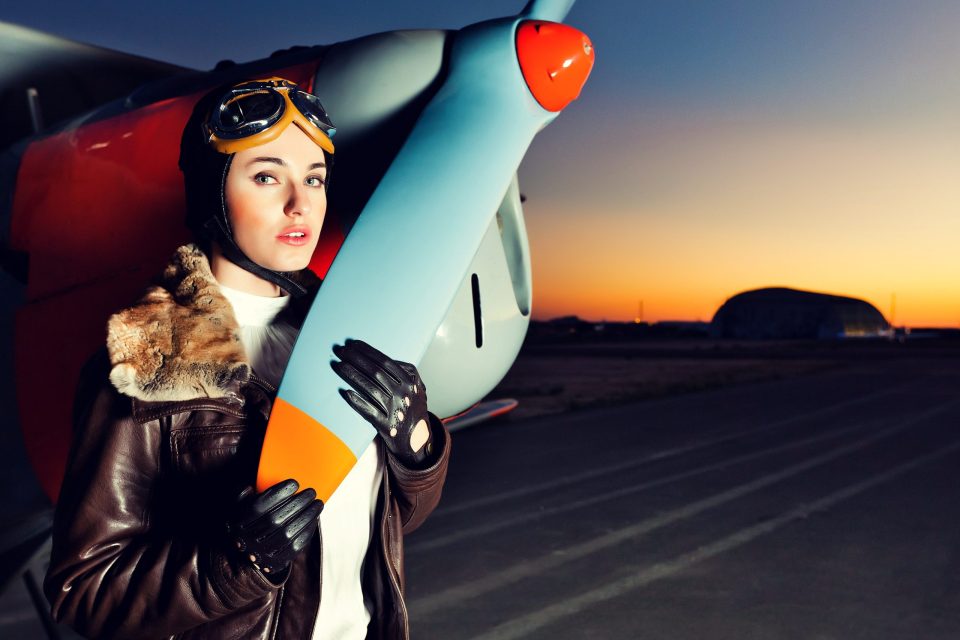 Retrato editorial al aire libre de una modelo con gafas de aviador, chaqueta de cuero con cuello de pelo y guantes negros.