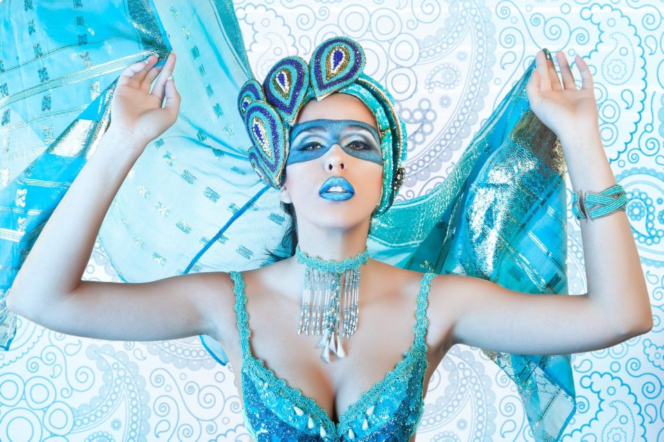Retrato editorial de fantasía y belleza de una modelo frente a un fondo con motivos ornamentales en tonos blancos y turquesa.