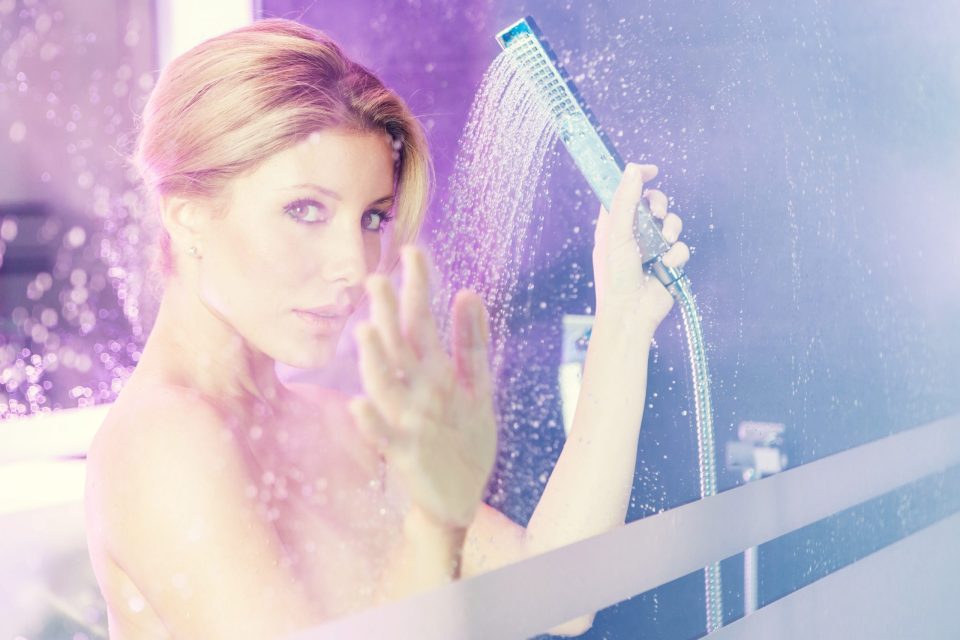 Retrato editorial de una mujer junto a una ducha, vista a través de un cristal con gotas de agua.