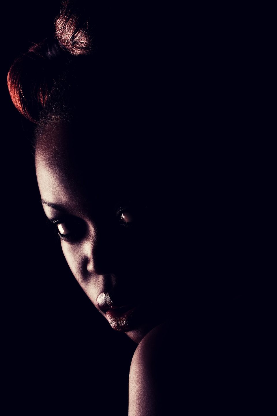 Retrato vertical de una modelo en primer plano, con el rostro inclinado y parcialmente oculto entre sombras.