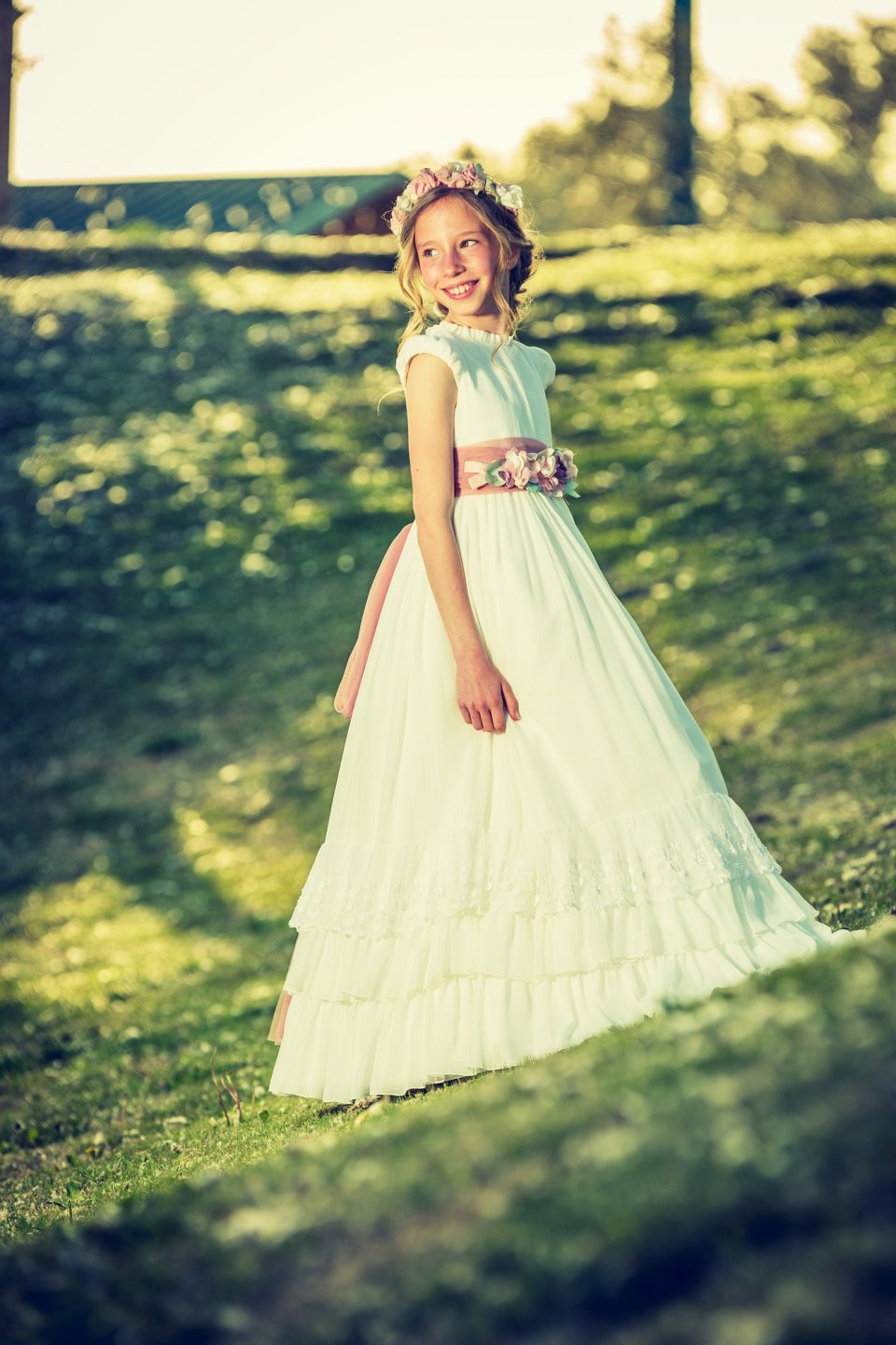 Retrato vertical de una niña en un parque, sonriente y mirando hacia un lado.