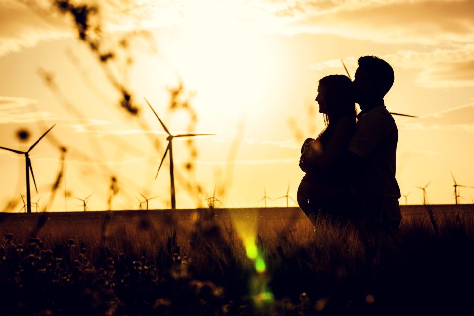 Silueta de una pareja abrazada en un campo de cultivo al atardecer.