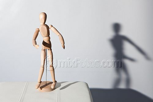 A jointed wooden mannequin stands on a light-coloured surface, lit from the left.
