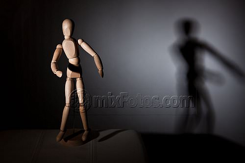 A wooden articulated mannequin stands on a dark surface, lit from the side.