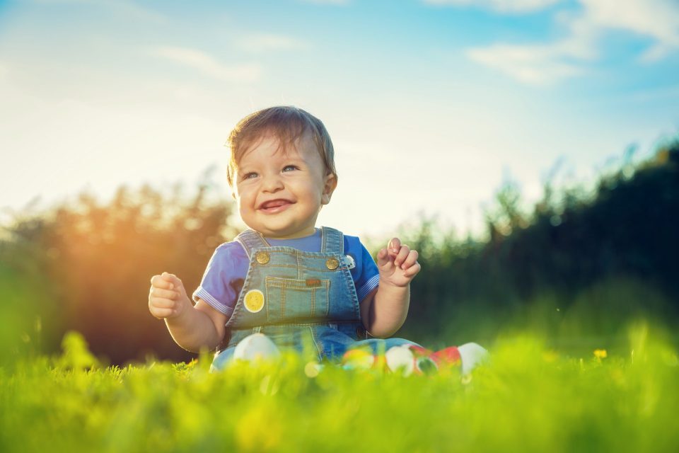 Un niño pequeño sonríe sentado sobre la hierba en un campo.
