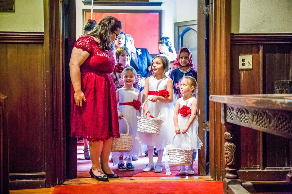 A woman in a red dress stands beside several girls and boys in a doorway.