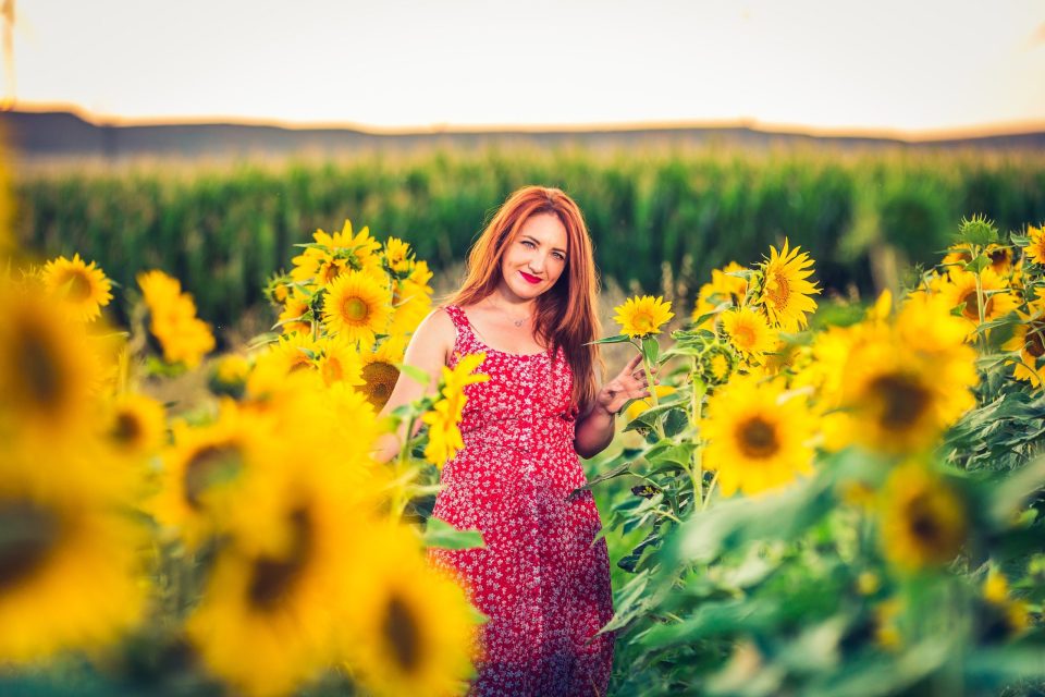A red-haired woman poses among tall sunflowers.