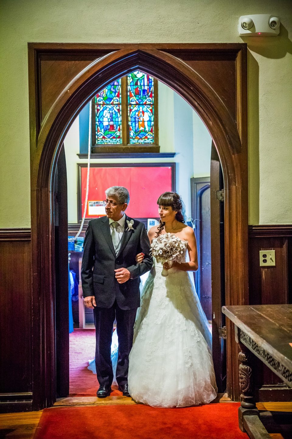A bride in a white dress and carrying a bouquet walks beside a man in a dark suit.