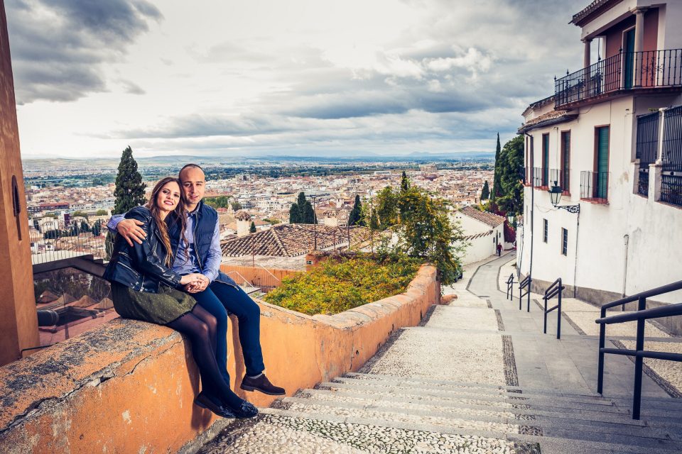 A couple sit on the side wall of a cobbled staircase.