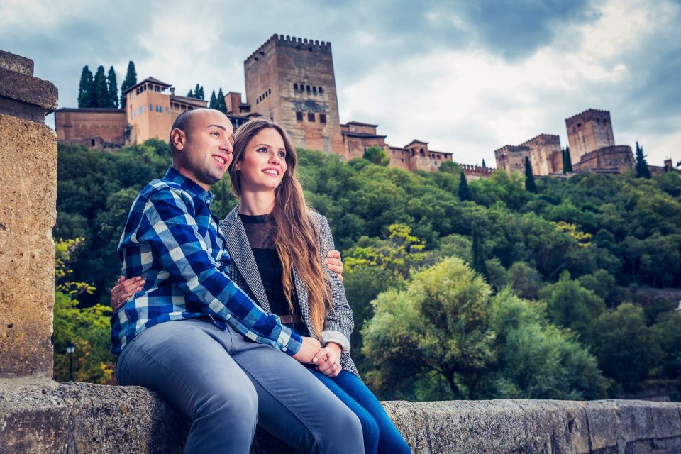 A couple sits embracing on a stone wall during a pre-wedding shoot in the city.