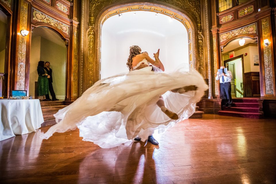 A couple dance in the centre of a wedding reception venue with ornate gold and wood-toned décor.