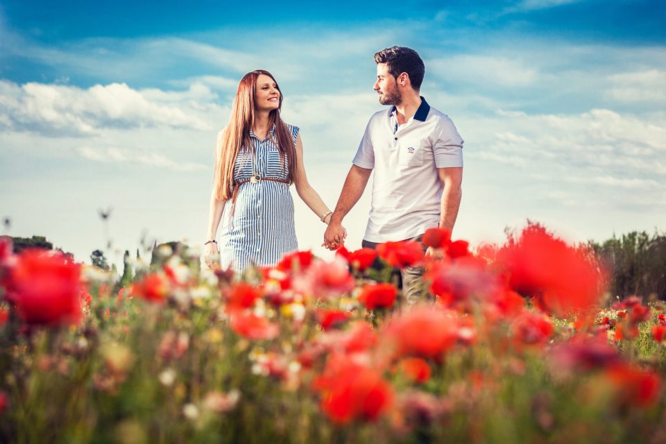 Una pareja camina de la mano entre amapolas rojas en un campo.