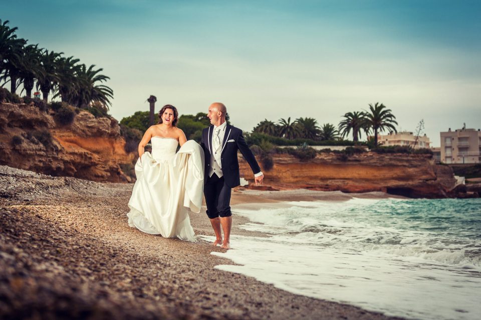 Una pareja camina por la orilla de una playa de piedras junto al mar.