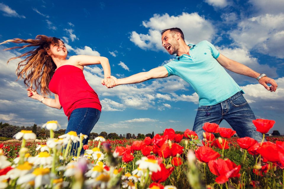 Una pareja corre y se sostiene de la mano en un campo florido.