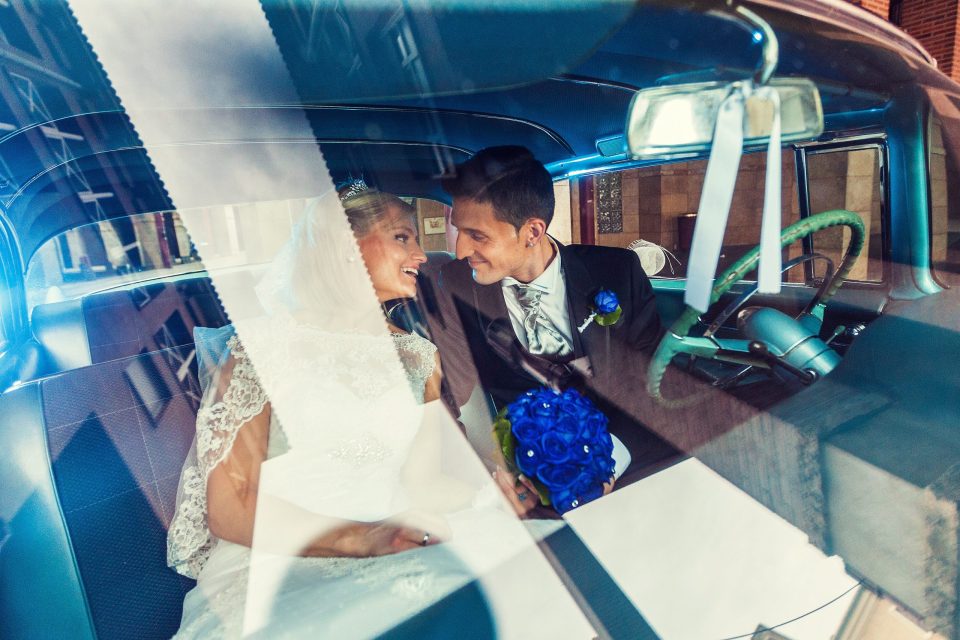 Una pareja de novios aparece sentada en el interior de un coche clásico azul.