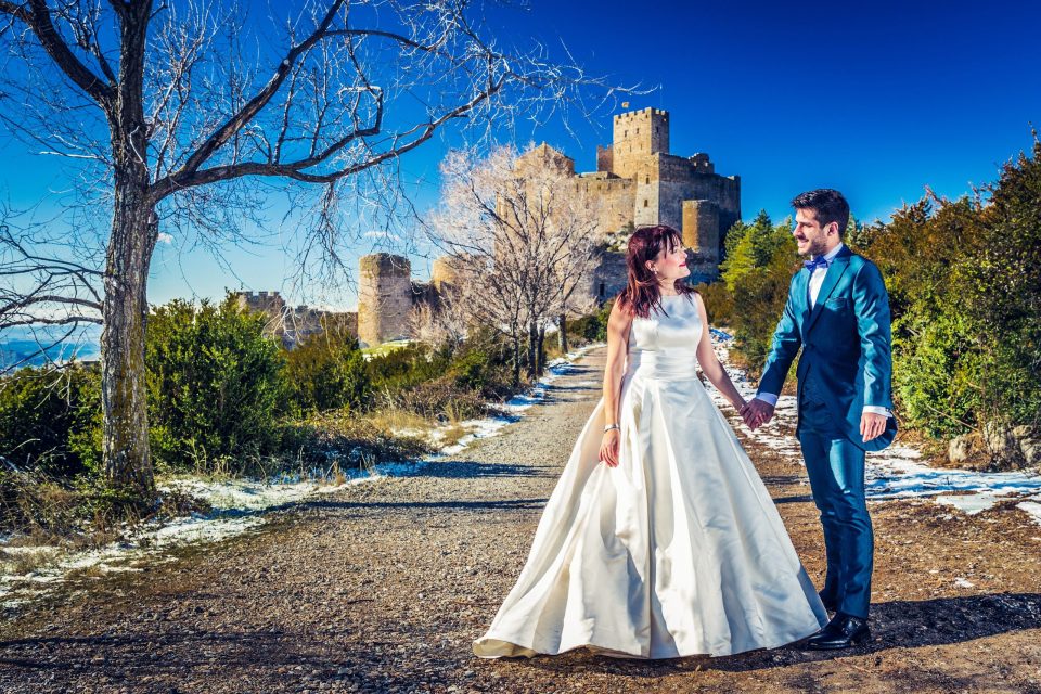 A bride and groom walk hand in hand along a path with patches of snow.