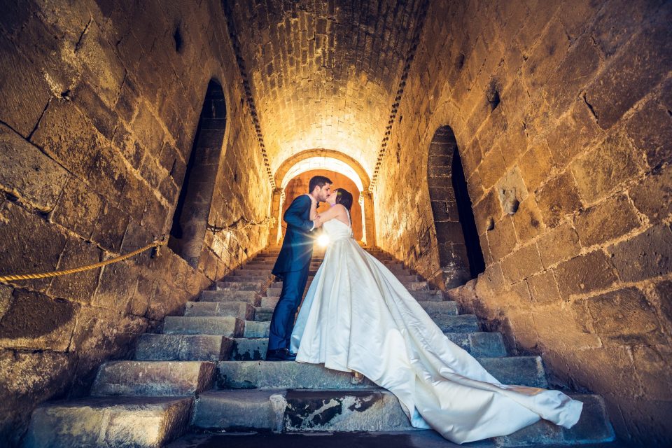 A bride and groom pose embracing on a stone staircase inside a church.