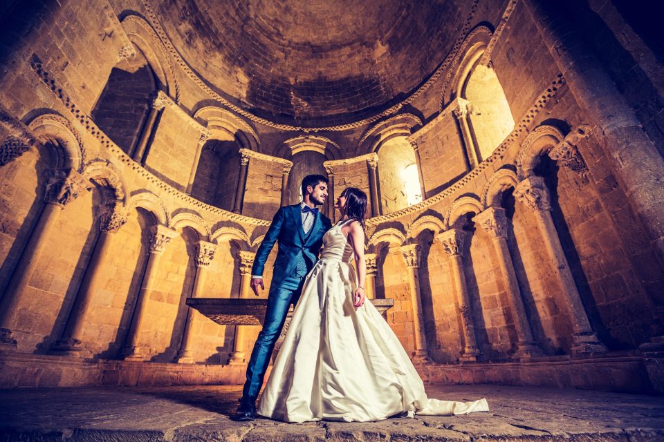 Una pareja de novios posa en el interior de una iglesia de piedra, bajo una cúpula decorada con arcos y relieves.