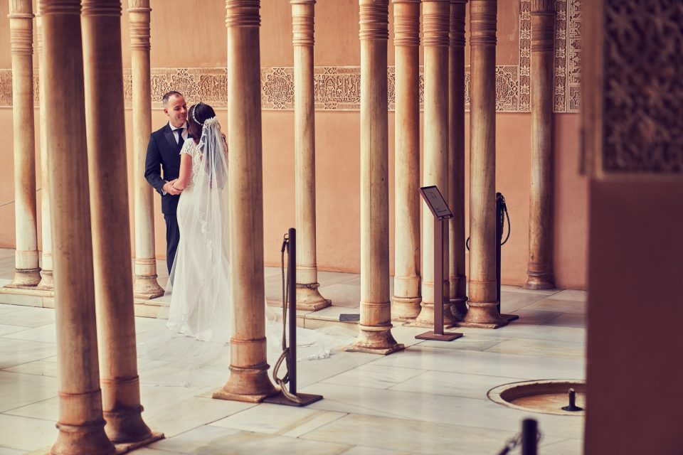 Una pareja de novios posa junta en el patio de un monumento, rodeada de columnas ornamentadas.
