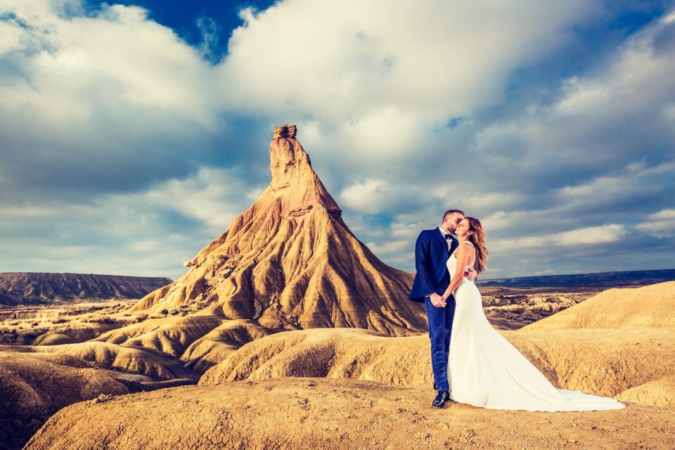 A newlywed couple pose and kiss beside a large eroded rock formation.