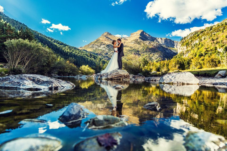Una pareja de novios se abraza y se besa sobre una roca junto a un río de montaña.
