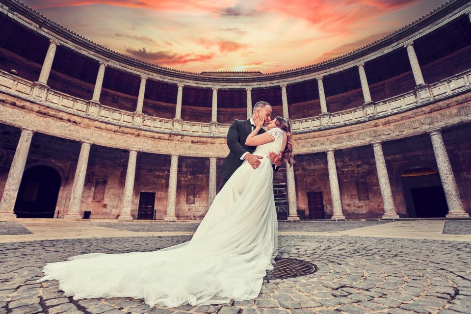 Una pareja de novios se besa en el patio circular de un monumento histórico rodeado de columnas y galerías.