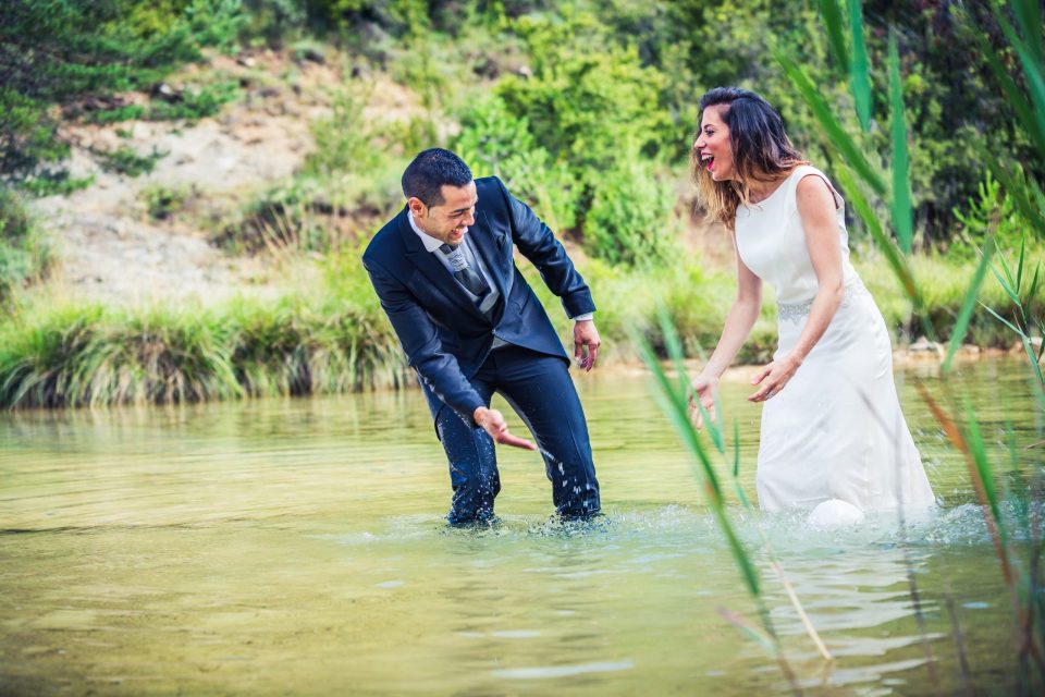 Una pareja de novios se divierte dentro de un río poco profundo rodeado de vegetación.