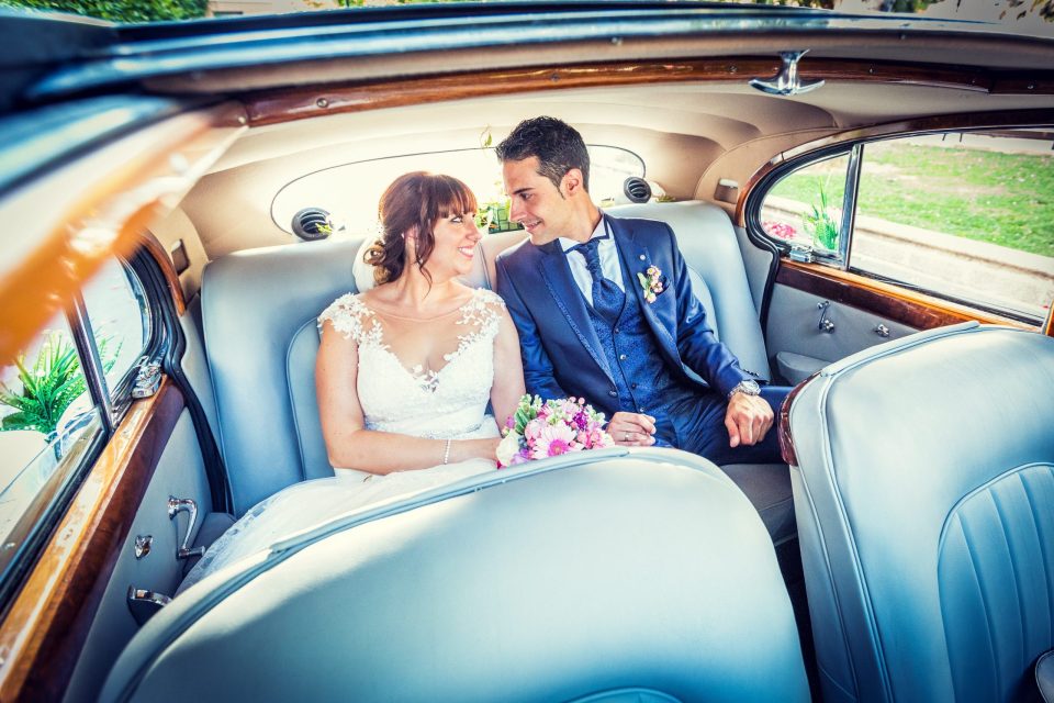 Una pareja de novios sentada en el asiento trasero de un coche clásico.