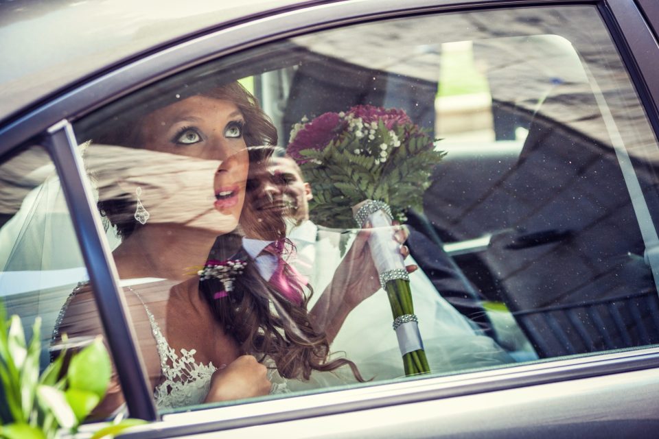 Una pareja de recién casados aparece dentro de un coche visto a través de la ventanilla.