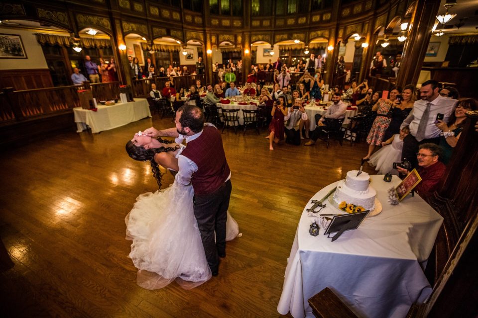 A newlywed couple dances in the centre of an ornate reception hall.