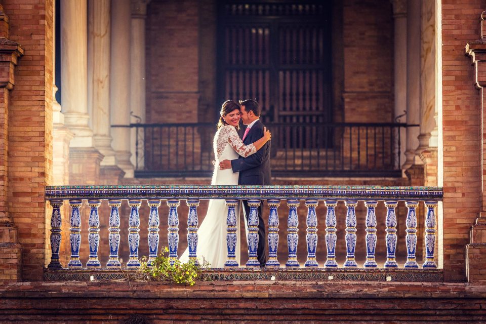 A newlywed couple embrace on a balcony decorated with blue and white tiles.
