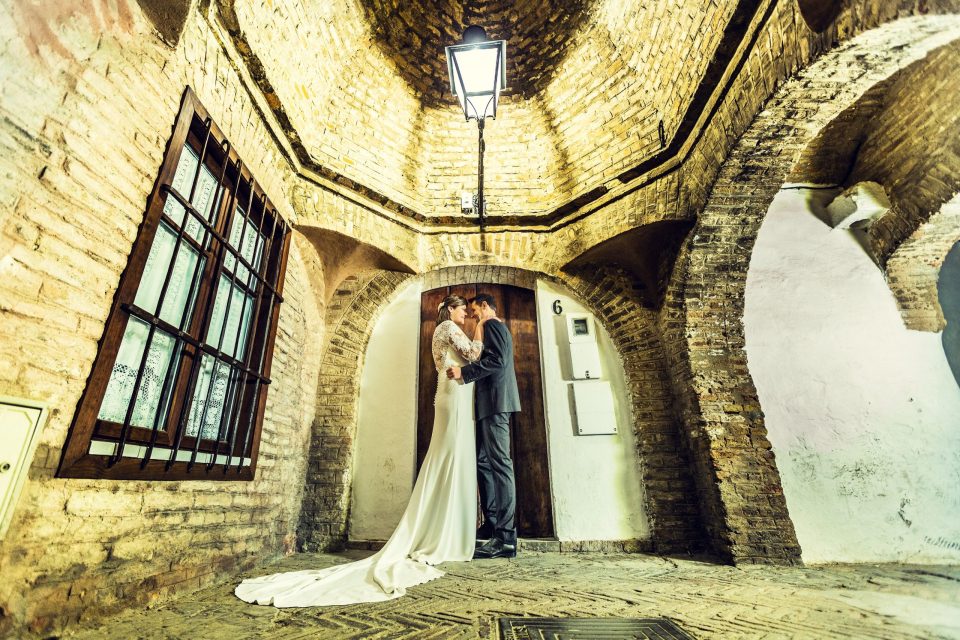 A newlywed couple embrace and kiss in front of a wooden door.