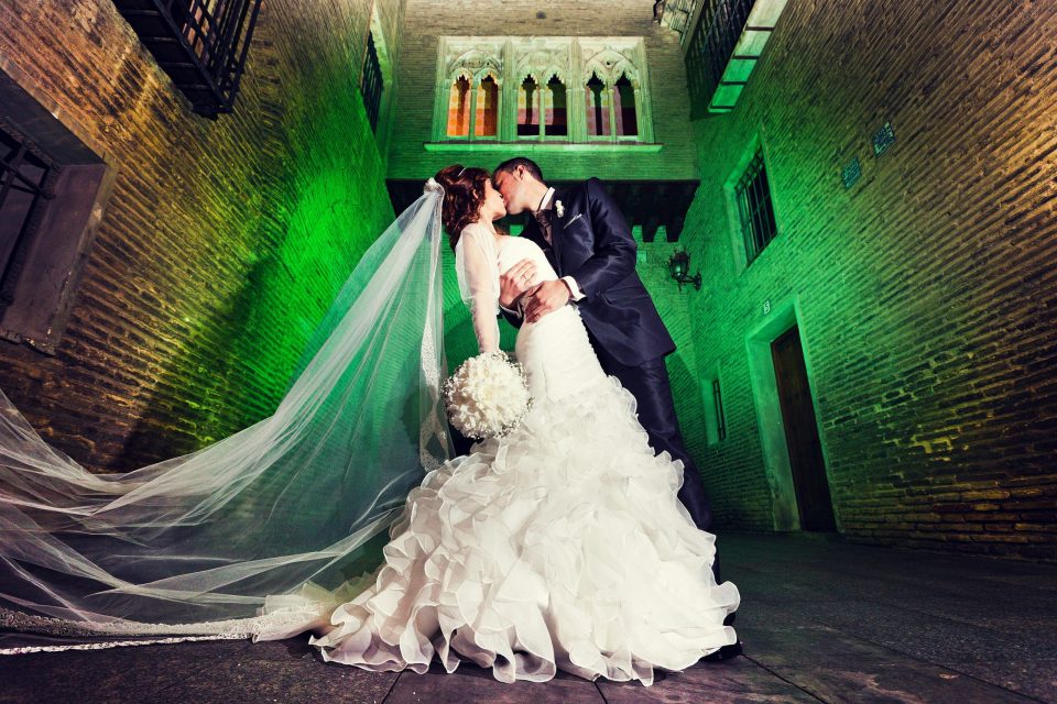 Una pareja de recién casados se besa en un pasaje de ladrillo iluminado con luz verde.