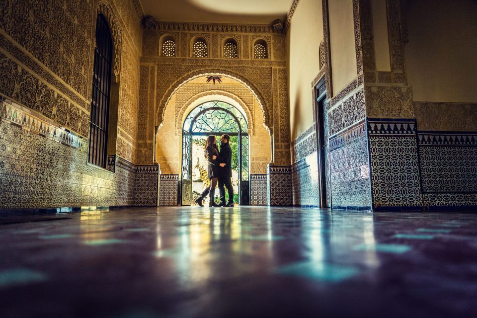A couple stand beside a large arched doorway inside an ornate building.