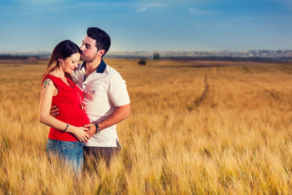 Una pareja posa en un campo de cereal dorado bajo un cielo azul.