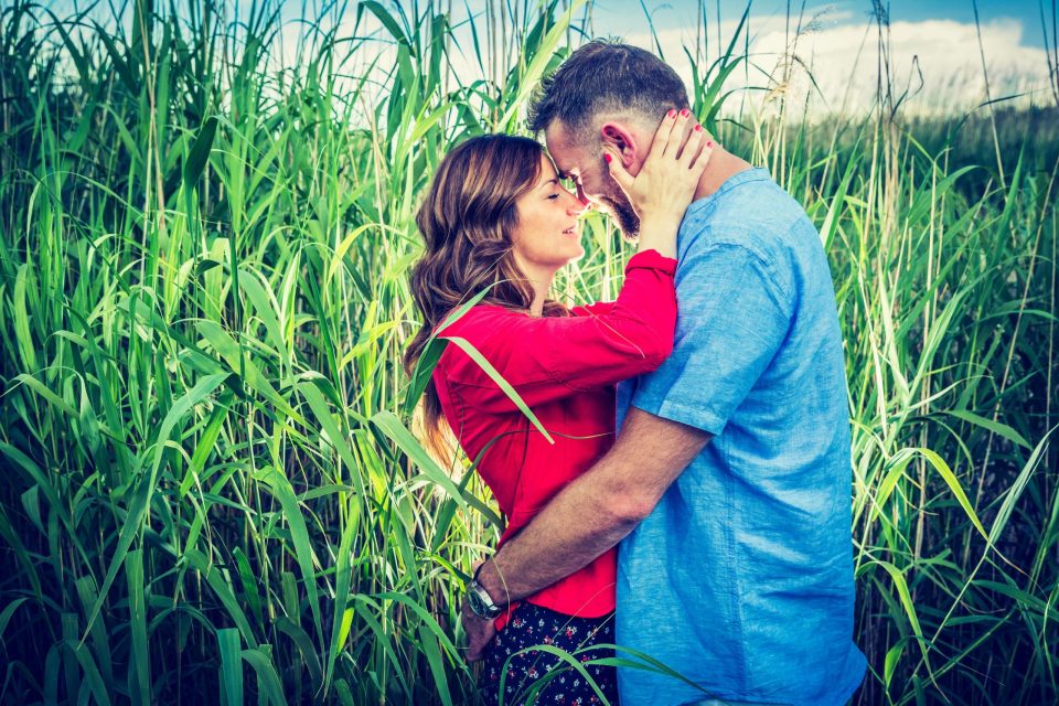 Una pareja posa en un entorno natural de parque, rodeada de plantas altas.