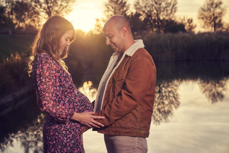 Una pareja posa junto a un estanque en un parque al atardecer.