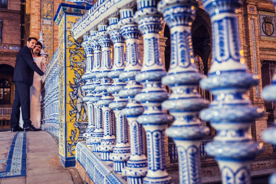 A couple poses beside a balustrade decorated with blue and white tiles.