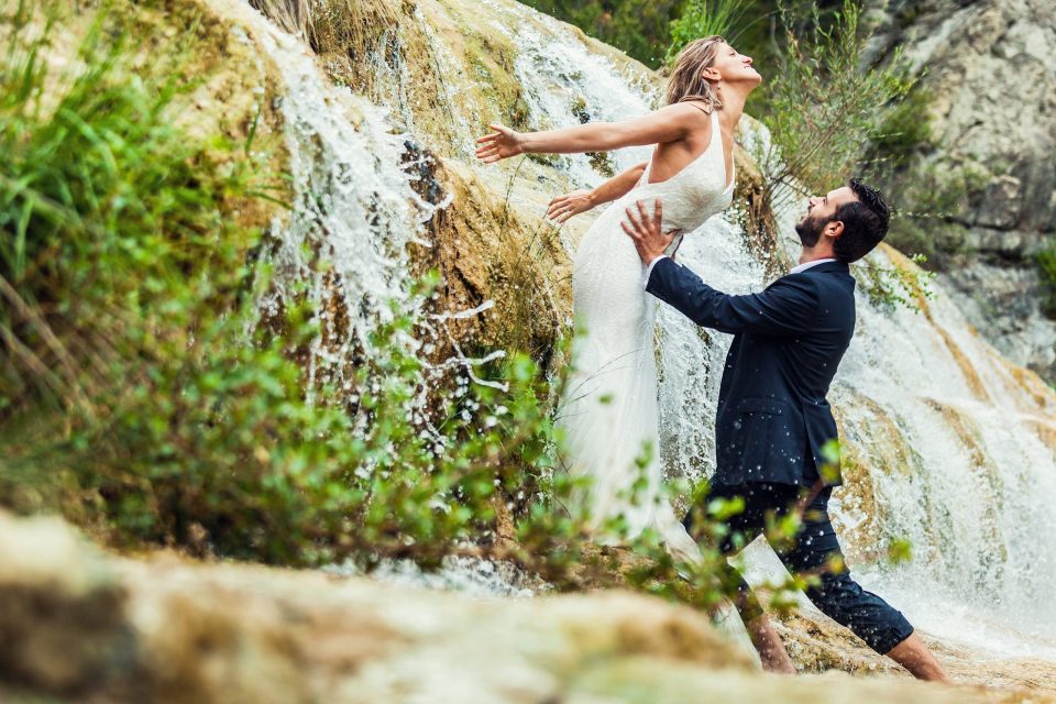 Una pareja posa junto a una cascada en un entorno natural.