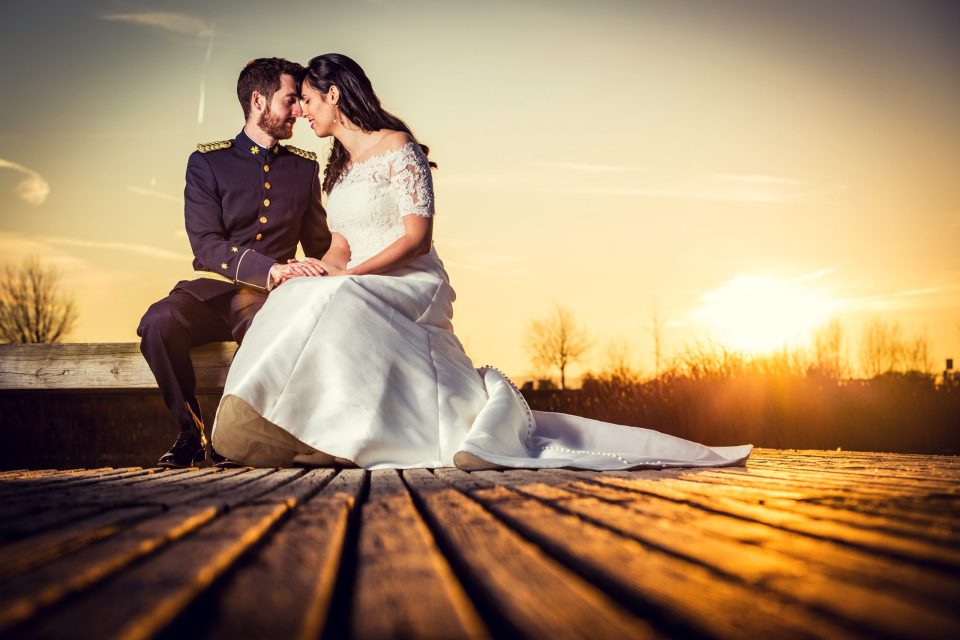 Una pareja posa sentada sobre un muelle de madera al atardecer.