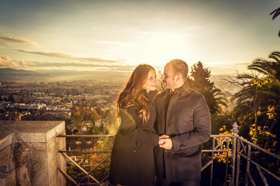 A couple embraces beside a railing at a lookout, illuminated by the golden evening light.
